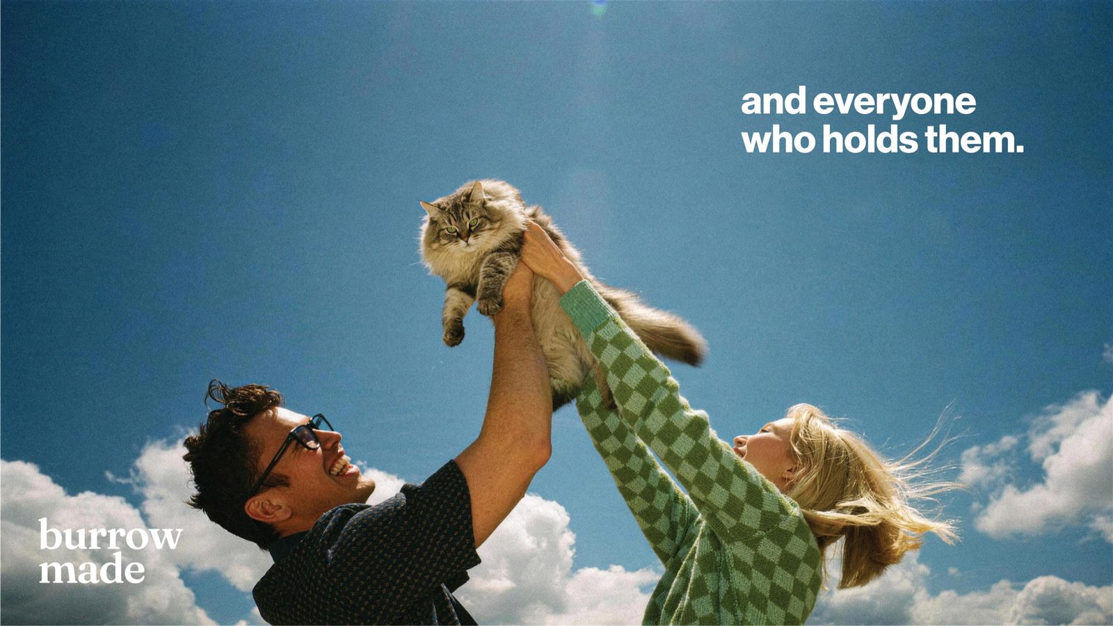 A couple holding their cat up in the sunshine